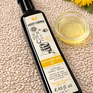 K&ouml;nnte beinhalten: Eine schwarze Flasche Green Farmer Sonnenblumenkern&ouml;l mit einem Etikett mit Illustrationen und Text. Eine kleine Glasschale mit &Ouml;l und eine Sonnenblume sind ebenfalls vorhanden. Die Flasche enth&auml;lt 250 ml &Ouml;l.