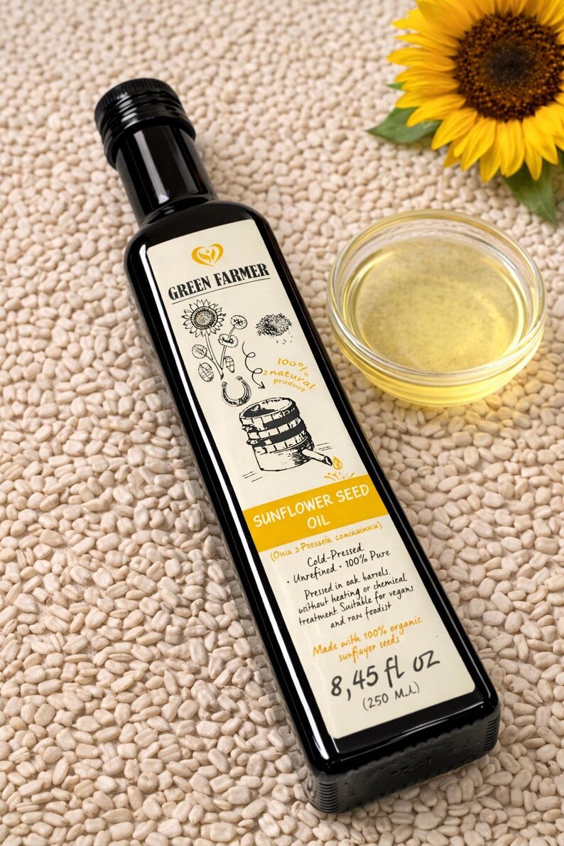 K&ouml;nnte beinhalten: Eine schwarze Flasche Green Farmer Sonnenblumenkern&ouml;l mit einem Etikett mit Illustrationen und Text. Eine kleine Glasschale mit &Ouml;l und eine Sonnenblume sind ebenfalls vorhanden. Die Flasche enth&auml;lt 250 ml &Ouml;l.