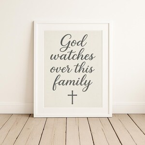 May include: A white framed print with the text "God watches over this family" in gray cursive lettering and a gray cross below the text.