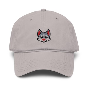 May include: A light gray baseball cap featuring an embroidered cartoon wolf face with gray fur, red ears, and a red nose. The cap has a curved brim and an adjustable strap at the back.