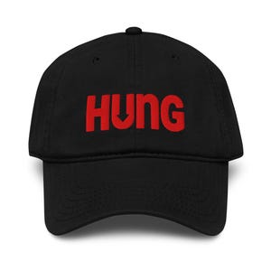 May include: Black baseball cap with the word "HUNG" embroidered in red across the front. The "U" in "HUNG" has a downward-pointing arrow. The cap has a curved brim and a button on top.