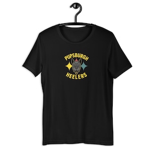 May include: Black t-shirt with a graphic featuring a dog wearing glasses and a party hat, with the text "Pupsburgh Heelers" in yellow. The design includes two starbursts in yellow and teal.