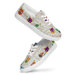 May include: A pair of canvas sneakers with a repeating pattern of cartoon dog faces in various colors and bone shapes on a light gray background. The shoes have white laces and white soles.