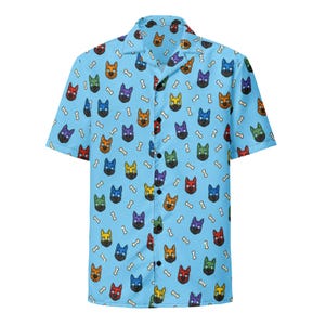 May include: A light blue short-sleeve button-down shirt featuring an all-over repeating pattern of stylized dog heads in various colors including red, orange, yellow, green, blue, and purple, interspersed with small white bone shapes.