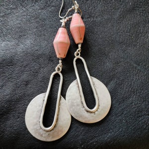 May include: A pair of silver dangle earrings with a pink and white geometric bead at the top of each earring.