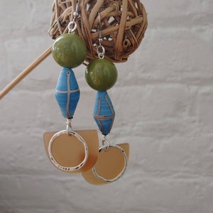 May include: A pair of dangle earrings with green and blue beads and a silver hoop. The earrings are hanging from a woven ball.