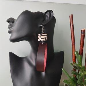 May include: A pair of dangle earrings with a brown leather strap and a white and black patterned cube. The earrings are on a black mannequin head.