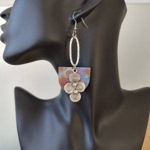May include: Silver dangle earrings with a half-circle shaped pendant featuring a multi-colored abstract design and a silver swirl design.