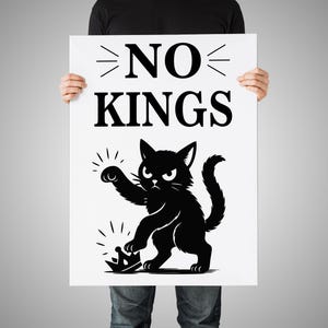 May include: A white poster with the words "NO KINGS" in bold black letters. Below the text is a black cat illustration, stepping on a crown. The cat has an angry expression. The poster is held by a person.