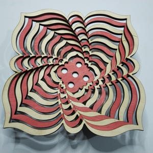 May include: A layered wooden art piece in a floral design. The piece features alternating layers of red, cream, and black, creating a three-dimensional effect. The center has a series of circular cutouts. The artwork is displayed against a white background.