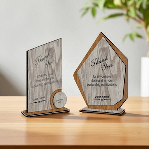 May include: Two wooden plaques with a light wood grain finish. Each plaque has the words "Thank You" and a message of appreciation. One plaque is rectangular, the other is a geometric shape.