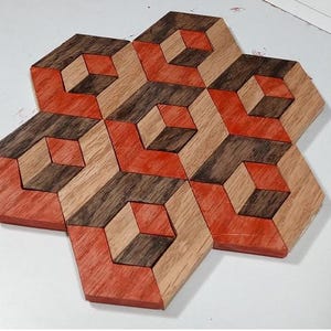 Könnte beinhalten: Ein Holzuntersetzer-Set mit geometrischem Design. Die Untersetzer bestehen aus Holz mit einer Kombination aus rot-orange, hellbraun und dunkelbraun. Das Design erzeugt eine 3D-Würfel-Illusion. Die Untersetzer sind sternförmig angeordnet.