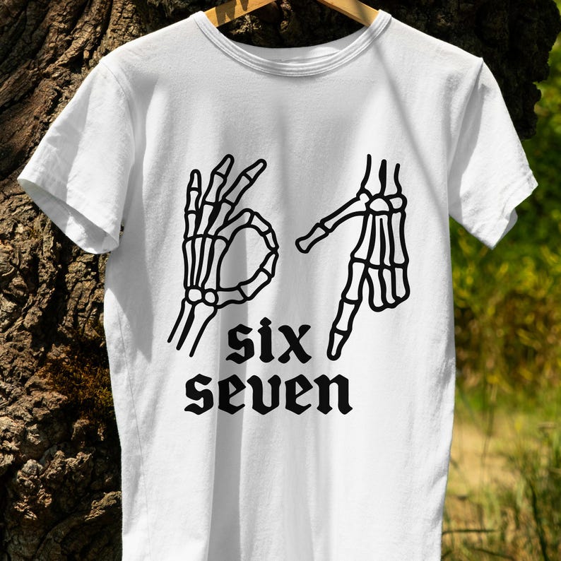May include: White t-shirt featuring a black graphic of two skeleton hands forming the numbers six and seven in American Sign Language. The words "six" and "seven" are printed below the hands in a gothic font.