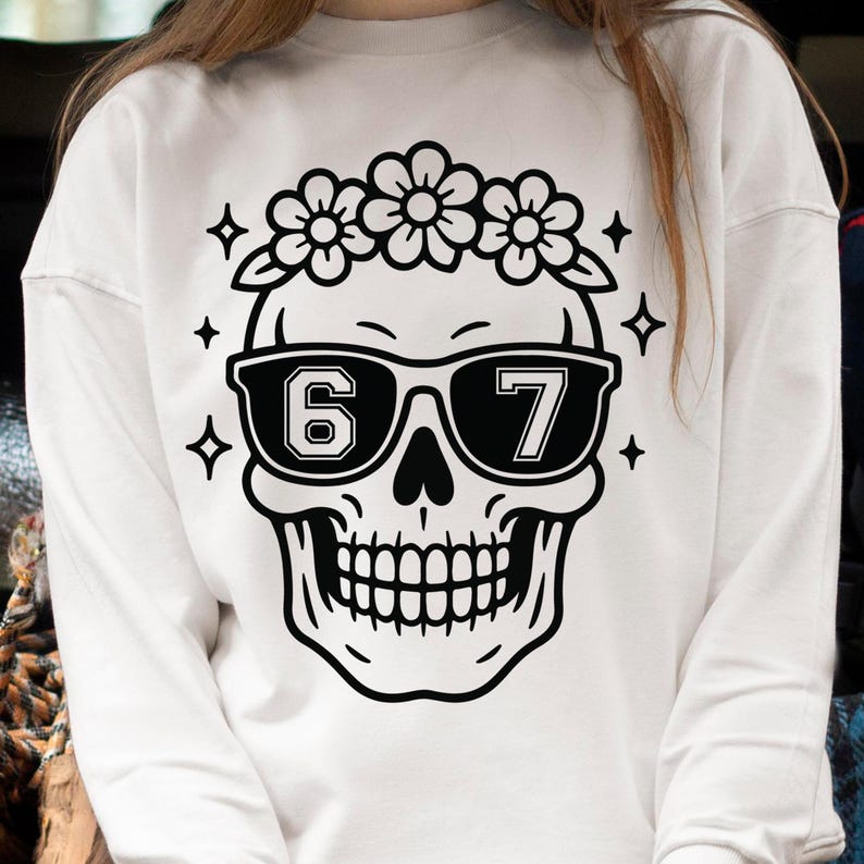 May include: White sweatshirt featuring a black and white skull design. The skull wears sunglasses with the numbers "67" and a floral crown. Four black diamond shapes and flowers surround the skull.