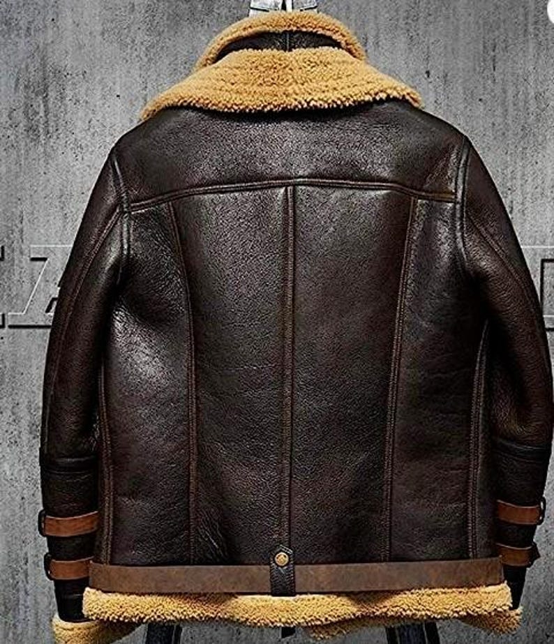 May include: A dark brown leather jacket with a tan shearling collar and lining. The jacket features a classic design with a belted waist, buckle details on the sleeves, and a button closure. The jacket is a medium weight and appears to be well-constructed.