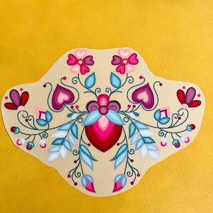 Peut inclure: Un motif floral beige avec des accents roses, violets et bleus. Le motif présente des fleurs stylisées, des cœurs et des feuilles, avec une forme de cœur centrale. Le fond est de couleur jaune uni.