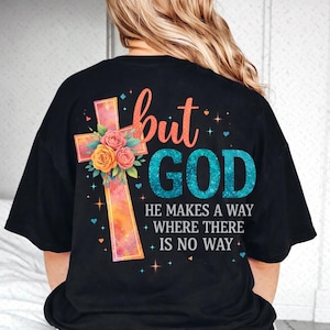 May include: Black t-shirt with a colorful cross design and the words "but GOD" in a script font. The cross is decorated with flowers and the text "HE MAKES A WAY WHERE THERE IS NO WAY".