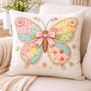 Könnte beinhalten: Ein dekoratives quadratisches Kissen mit einem Schmetterlingsdesign. Der Schmetterling hat Patchwork-Flügel mit rosa, blauen, gelben und grünen Abschnitten, verziert mit Blumen, Erdbeeren und einer rosa Schleife. Das Kissen liegt auf einem cremefarbenen Sofa.