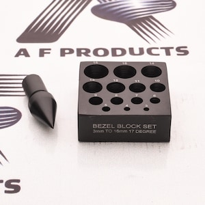 May include: A black metal bezel block set with a matching punch tool. The block features numbered circular indentations ranging from 3mm to 16mm. The front of the block is printed with the text BEZEL BLOCK SET 3mm TO 16mm 17 DEGREE.