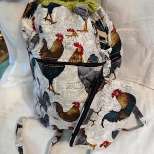 May include: A white drawstring bag with a green polka dot lining and a rooster print. The bag has a zippered pocket and a long strap. The bag is made of fabric and has a rooster print.