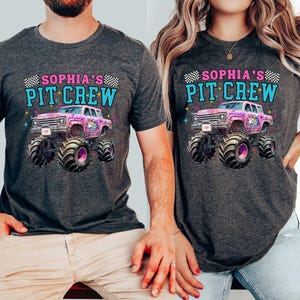 May include: Two dark gray t-shirts with the text "SOPHIA'S PIT CREW" above a graphic of a pink monster truck with a unicorn design. The monster truck has large black tires. The shirts are short-sleeved.
