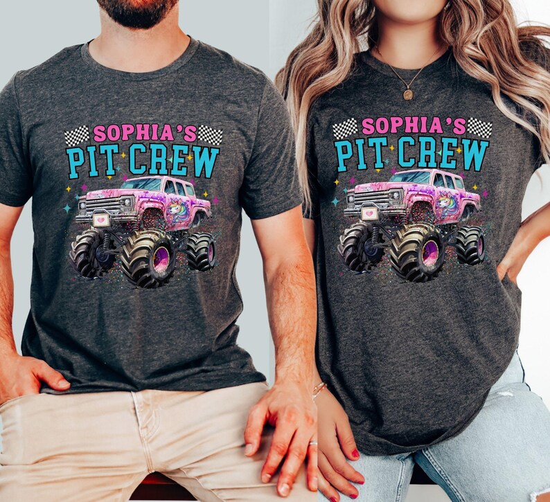 May include: Two dark gray t-shirts with the text "SOPHIA'S PIT CREW" above a graphic of a pink monster truck with a unicorn design. The monster truck has large black tires. The shirts are short-sleeved.