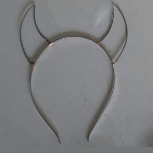 May include: A silver headband with two wire horns attached to the top. The horns are bent into a curved shape.