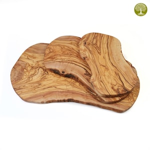 Pode incluir: Um conjunto de três tábuas de corte de madeira de oliveira com bordas naturais. As tábuas exibem uma cor castanho-clara e quente com padrões de grão de madeira únicos. De tamanhos e formas variadas, adequadas para a cozinha.