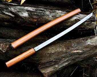 May include: A katana sword with a wooden handle and a silver blade, resting on a pile of tree branches.