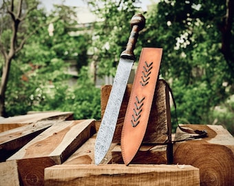 May include: A silver-coloured sword with a wooden handle and a leather sheath with decorative stitching. The sword and sheath are resting on a stack of wooden planks.