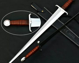 May include: A silver sword with a brown leather handle and scabbard. The sword has a double-edged blade and a pointed tip. The scabbard has a leather strap and a metal buckle.