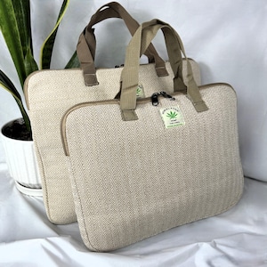 May include: Two beige laptop bags with brown handles and zippers. The bags have a herringbone pattern and a tag that reads "Himalayan Hemp The Tree". The bags are made of a natural-looking fabric.