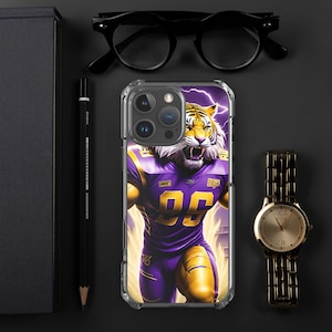 Könnte beinhalten: Eine transparente Handyhülle mit einem lila und goldenen Tiger, der ein Fussballtrikot trägt. Der Tiger hat einen Blitz hinter sich und die Nummer 99 auf seinem Trikot. Die Hülle ist für ein iPhone konzipiert.