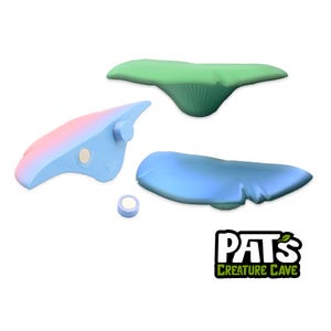 May include: Three colorful, abstract shapes in blue, pink, and green, along with a small, round magnet. The shapes appear to be stylized, possibly for a craft or art project. The logo "Pat's Creature Cave" is in the bottom right corner.