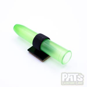 May include: A green plastic tube with a black 3D printed ring attached to a black base. The base has a circuit board design.