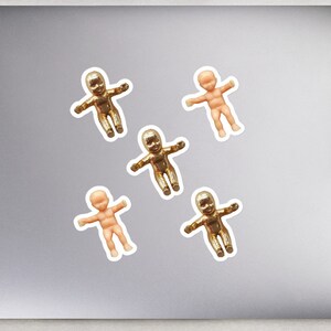 May include: Five small plastic baby dolls, four are gold and one is a natural skin tone. The dolls are arranged on a laptop computer.