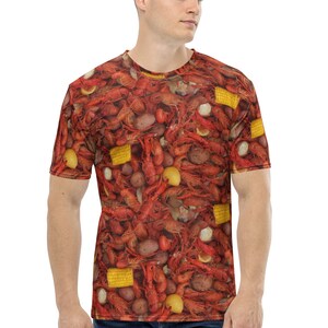 May include: A red t-shirt with a full-coverage print of crawfish, potatoes, corn, and lemons. The shirt is a casual style with short sleeves and a crew neck.
