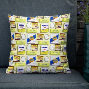 May include: A yellow throw pillow with a repeating pattern of various baking ingredients, including butter, sugar, flour, and active dry yeast. The pattern also includes white eggs.