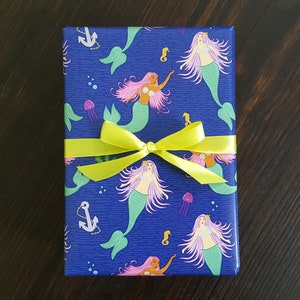 May include: A blue gift wrap with a mermaid pattern. The mermaids are pink and green with long hair and tails. The wrapping paper has a yellow ribbon tied around it.