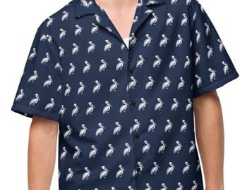 May include: A navy blue button-down shirt with a white pelican pattern. The short-sleeved shirt is paired with light blue shorts. The model is smiling and looking at the camera.