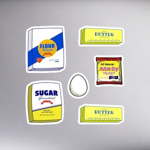 May include: A set of six stickers featuring various baking ingredients, including flour, sugar, butter, and yeast. The stickers are yellow and blue with white text and are on a silver laptop.