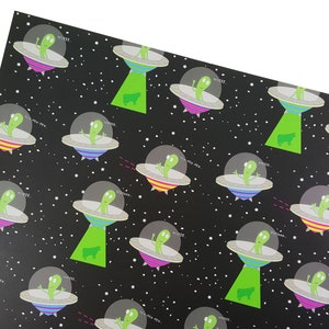 May include: Black and white wrapping paper with a repeating pattern of green aliens in flying saucers. The aliens are saying "MIIKEE" and "NEW-PEW-NEW". There are also green cows on the paper.
