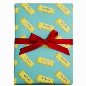 May include: A wrapped gift with a teal background featuring a repeating pattern of yellow butter sticks with the word "BUTTER" printed on them. The gift is tied with a red ribbon and bow.