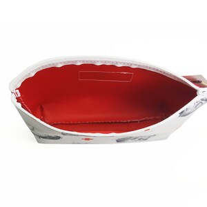 May include: White zippered pouch with a red interior and a white and grey print of small animals. The pouch is open and the zipper is pulled down.