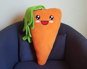 May include: A plush carrot-shaped pillow with a green leafy top and a smiling face. The pillow is sitting on a blue armchair.