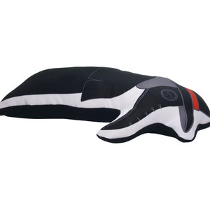 May include: Black and white plush pillow shaped like a dachshund dog. The dog is lying down with its head turned to the side. The pillow has a red stripe around the neck and a grey nose.