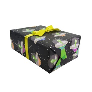 May include: A black gift box with a yellow ribbon. The box is wrapped in paper with a pattern of green aliens in flying saucers against a black background with white stars.