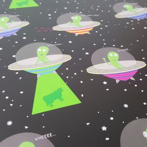 May include: A black background with a repeating pattern of green aliens in flying saucers. The aliens are saying different phrases like "Wheee...", "Pew Pew Pew", "Hiiiiieeee...", "Ooooo...", and "Wheeee..."  The aliens are green with black eyes and mouths. The saucers are gray with colorful stripes. There are white stars and triangles scattered across the background.