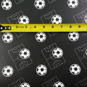 Puede incluir: Una cinta m&eacute;trica amarilla con marcas negras se coloca sobre un fondo negro con un patr&oacute;n repetido de balones de f&uacute;tbol blancos y campos de f&uacute;tbol. La cinta indica "2 FT & IN 3 4 5 6 7 8 9 10 1".