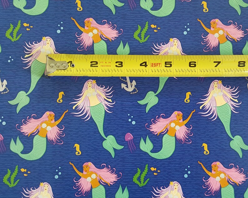 May include: A blue fabric with a repeating pattern of mermaids with pink hair and green tails. The fabric is measured with a yellow tape measure.